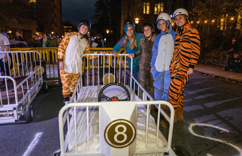 Four Lehigh students dressed up in costumes stand on Packer Ave next to a bed-shaped car