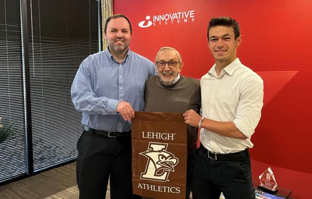 Bob Colonna, Thomas Duffy, and Robin Maillard standing together holding a brown Lehigh flag