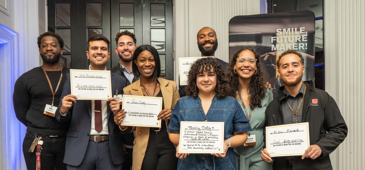 A group of Lehigh University young alumni pose for a group photo at an event while holding up individual cards they filled out