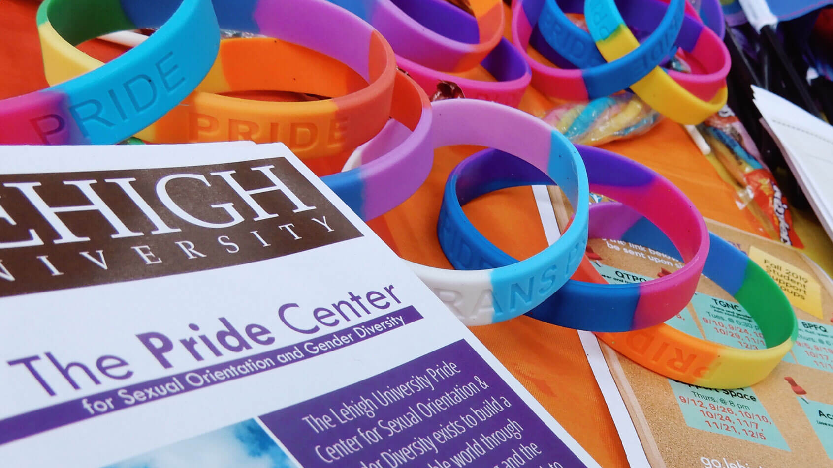 A promotional flyer for the Lehigh University Pride center resting on colorful silicone bracelets