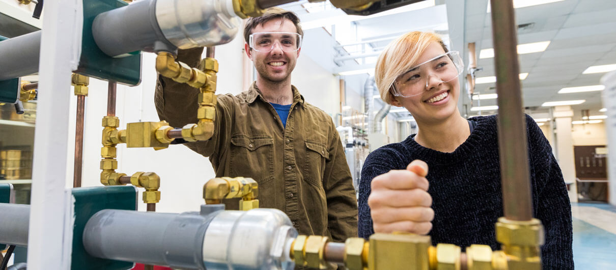 Students standing and smiling behind piping