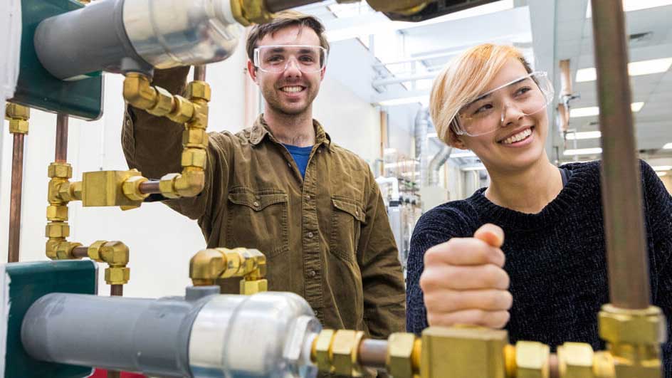 Students standing and smiling behind piping