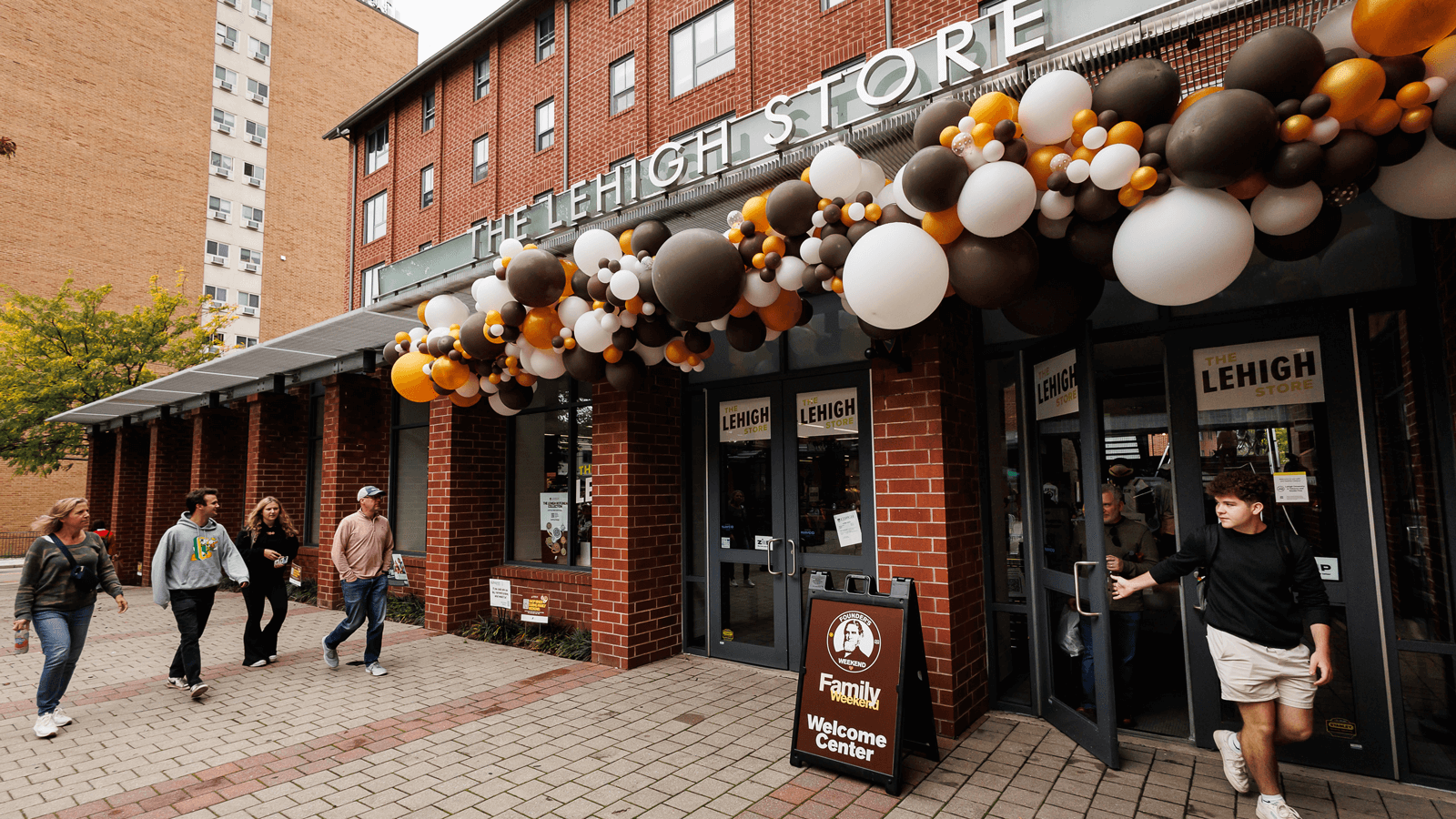 Exterior view of The Lehigh Store decorated in brown, orange, and white balloons with people approaching and one person walking out