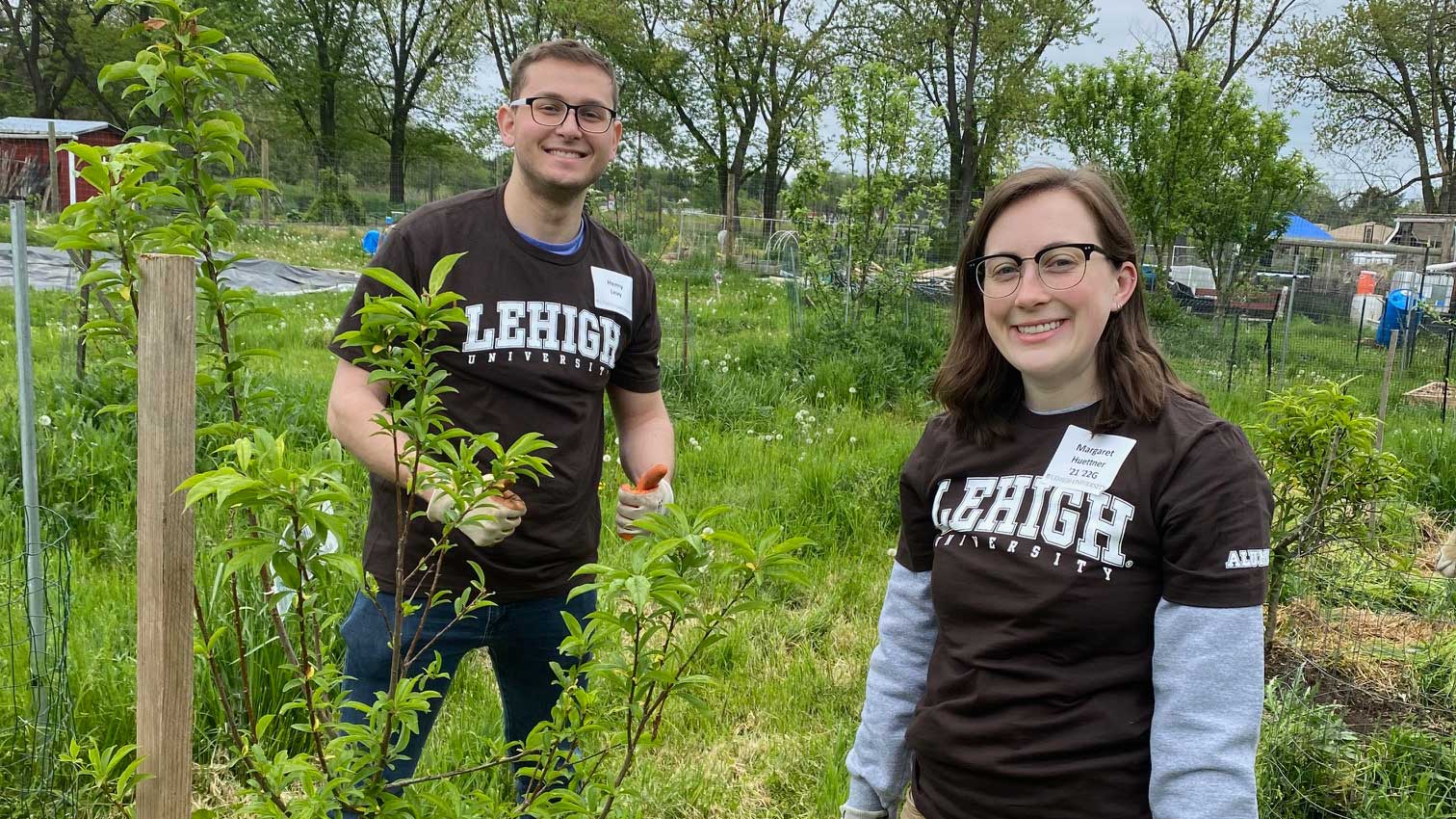 Two alumni wearing brown Lehigh shirts help to plant foliage.