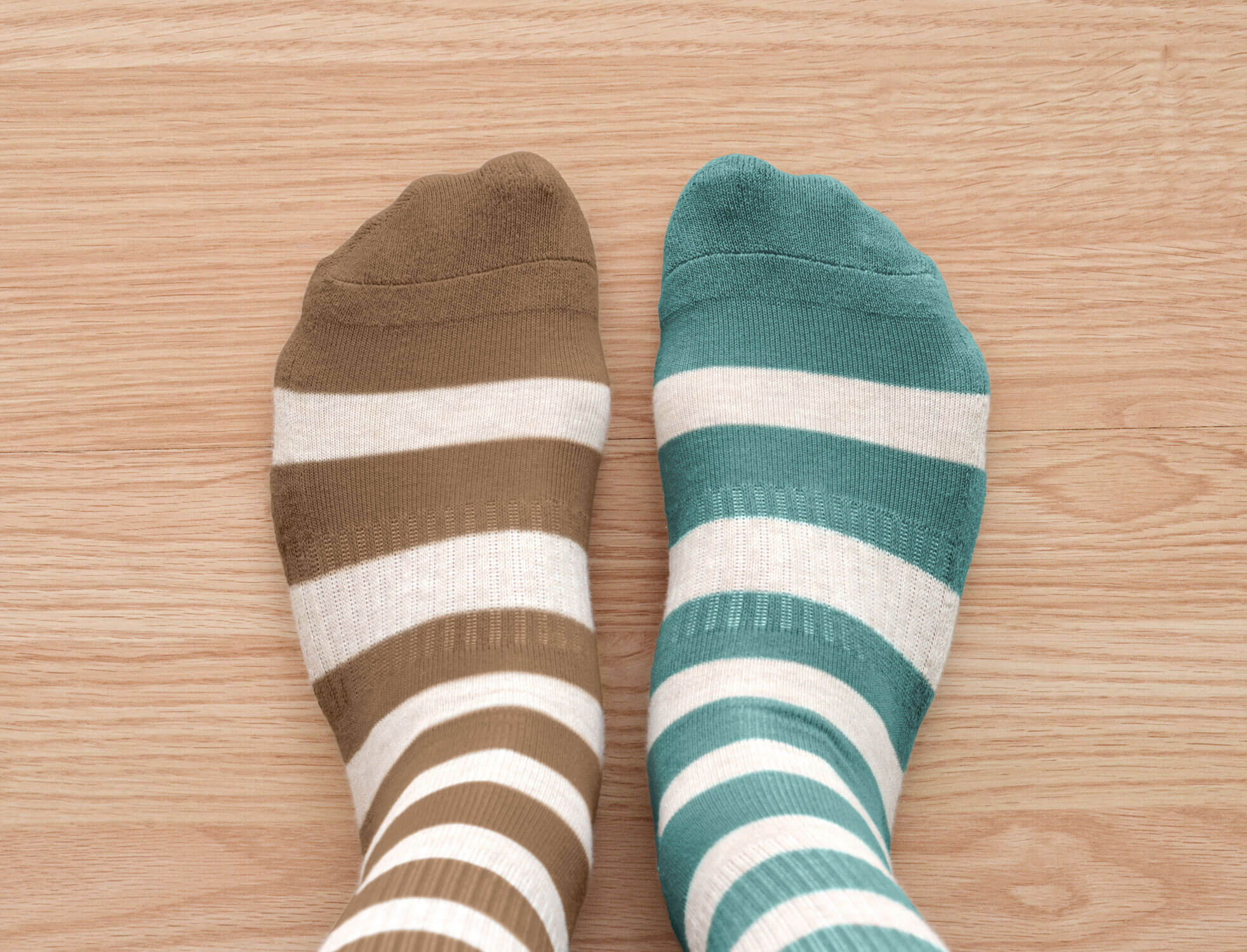 Two feet wearing brown and green mismatched, striped socks 