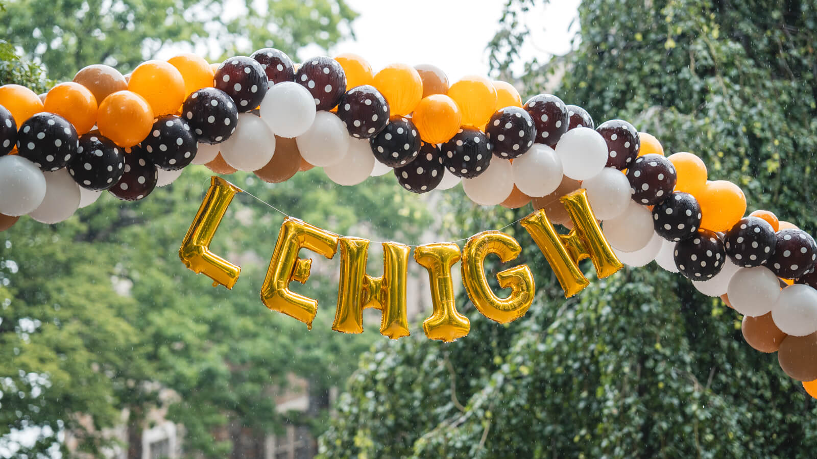 A brown, white, and orange balloon arch with gold foil letters spelling "LEHIGH" hanging underneath.