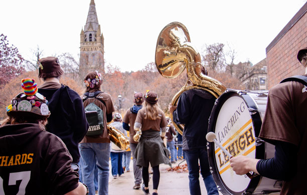 A rear view of the Lehigh University Marching Band walking away from the camera towards Lehigh's campus.
