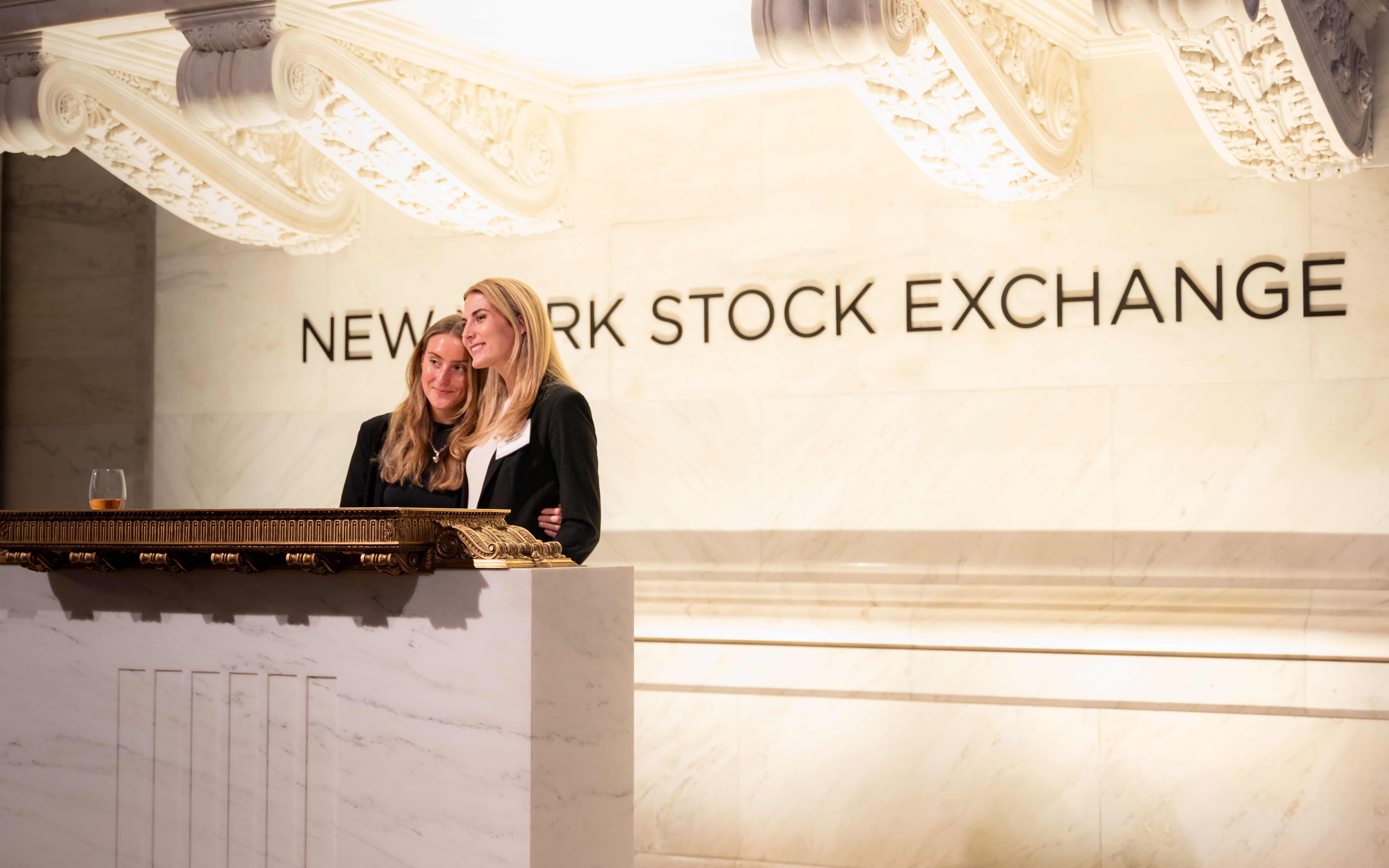 Two women stand in an embrace behind a podium at the New York Stock Exchange.