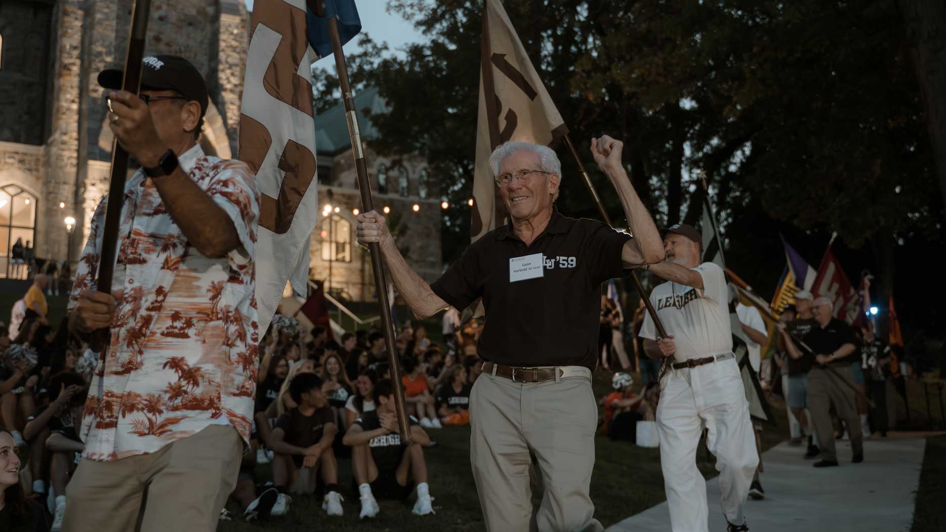 Alumni holding their class flags and walking past students on the Clayton UC Lawn.