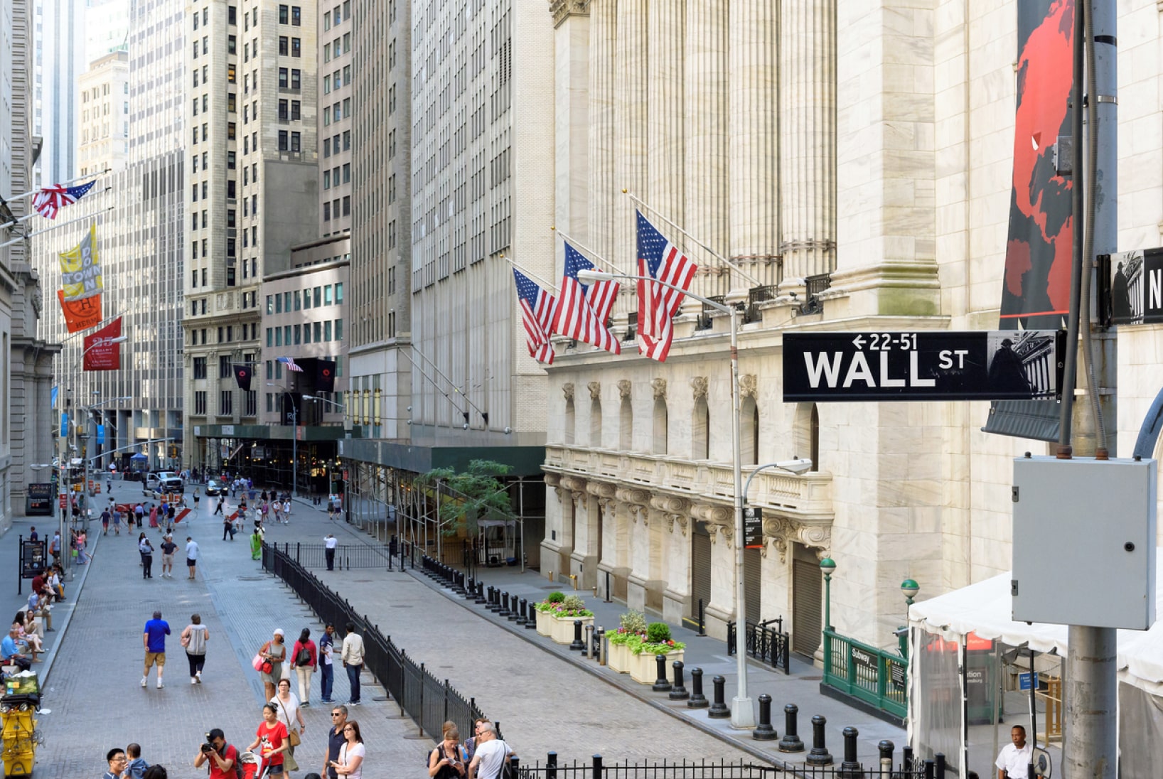 The road of Wall Street running past light stone buildings.