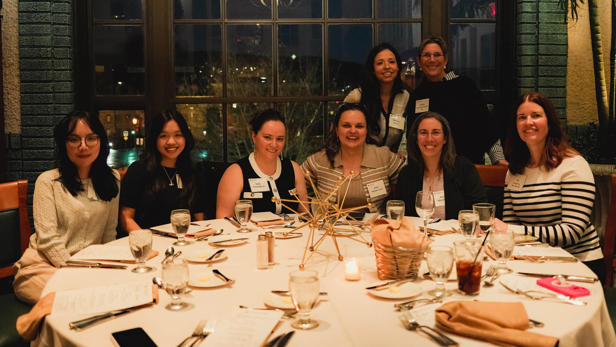A group of women smile for a photo while seated around a circular dinner table at a Lehigh University alumni event.