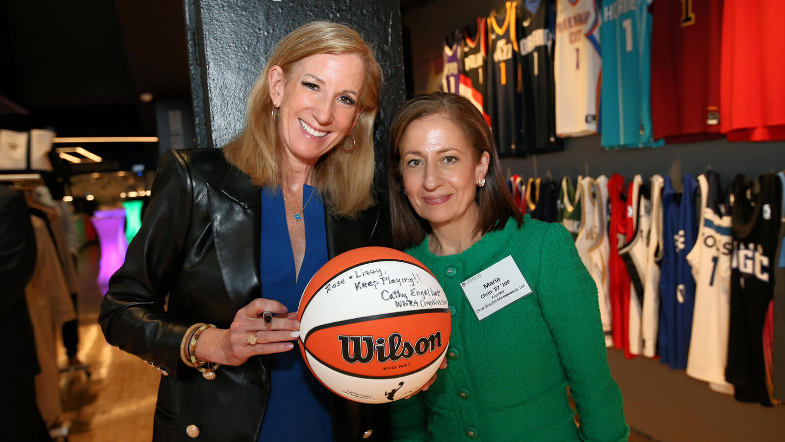 Cathy Engelbert poses with Maria Chrin after autographing a basketball she is holding with a Sharpie marker.