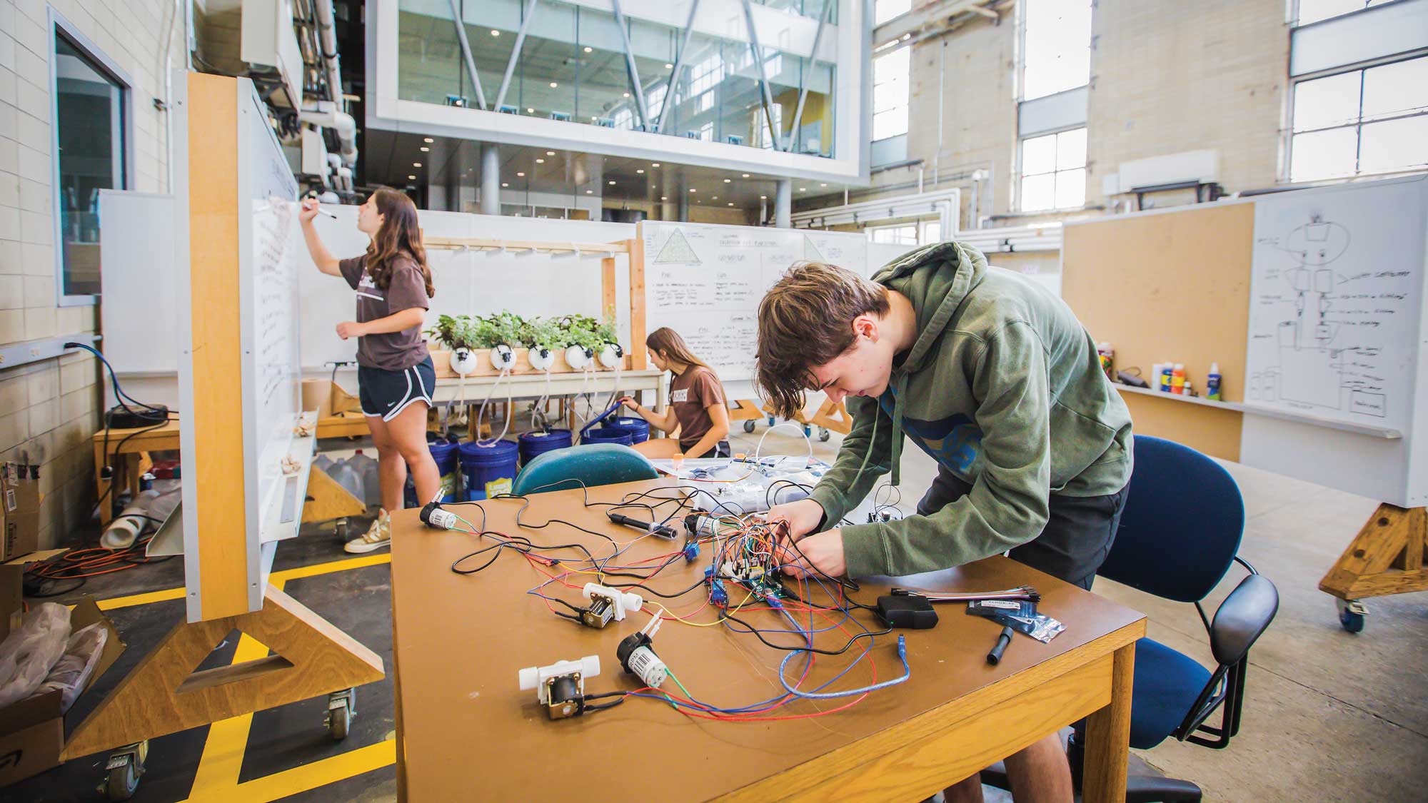 Lehigh students work on engineering projects in a spacious, high-ceilinged workshop space with whiteboards and hydroponic equipment.