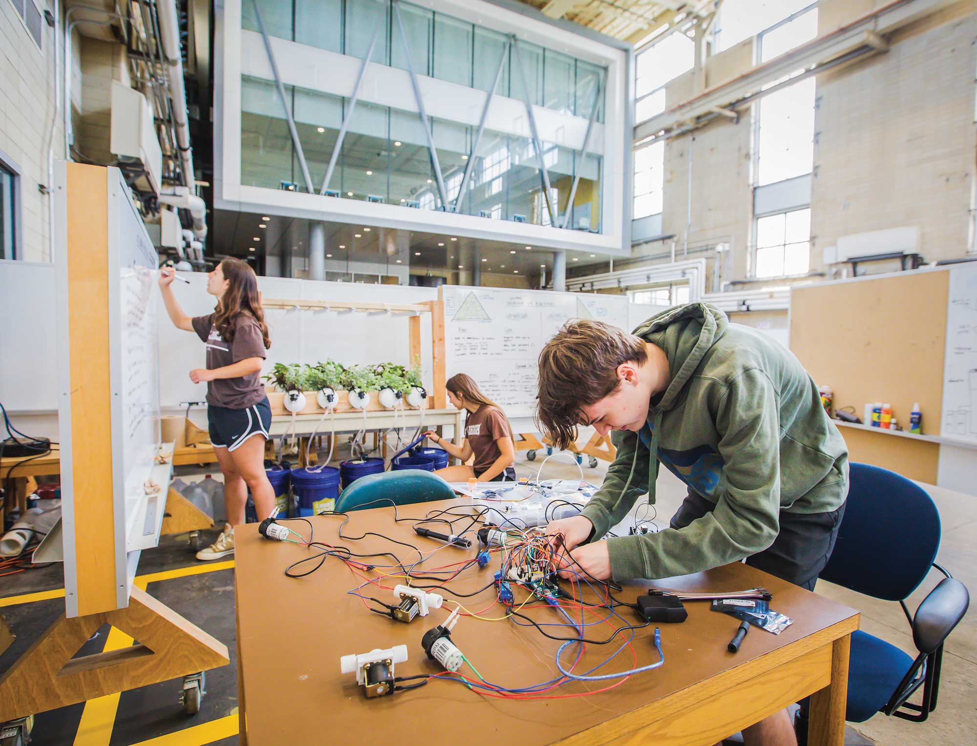 Lehigh students work on engineering projects in a spacious, high-ceilinged workshop space with whiteboards and hydroponic equipment.