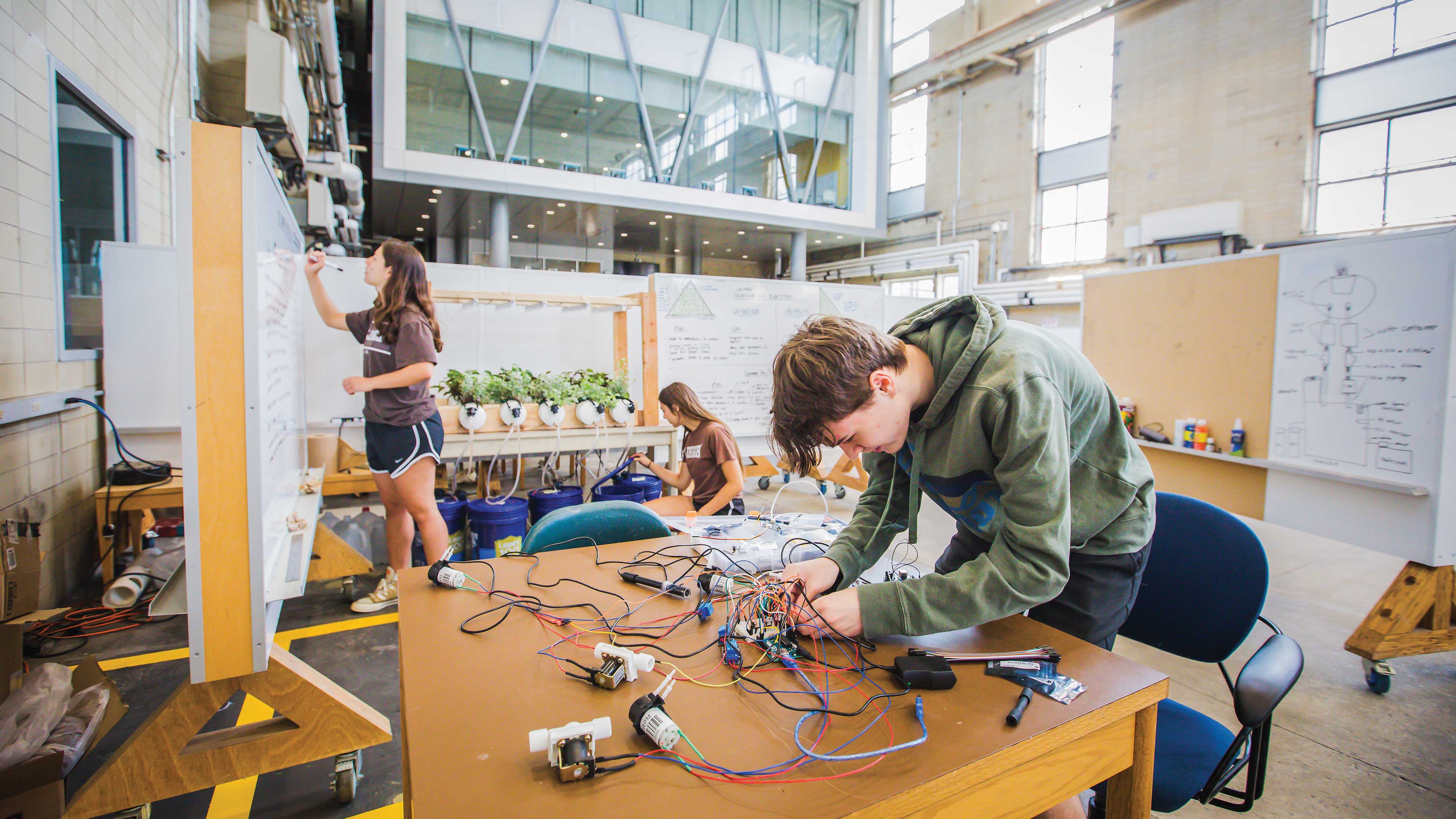 Lehigh students work on engineering projects in a spacious, high-ceilinged workshop space with whiteboards and hydroponic equipment.