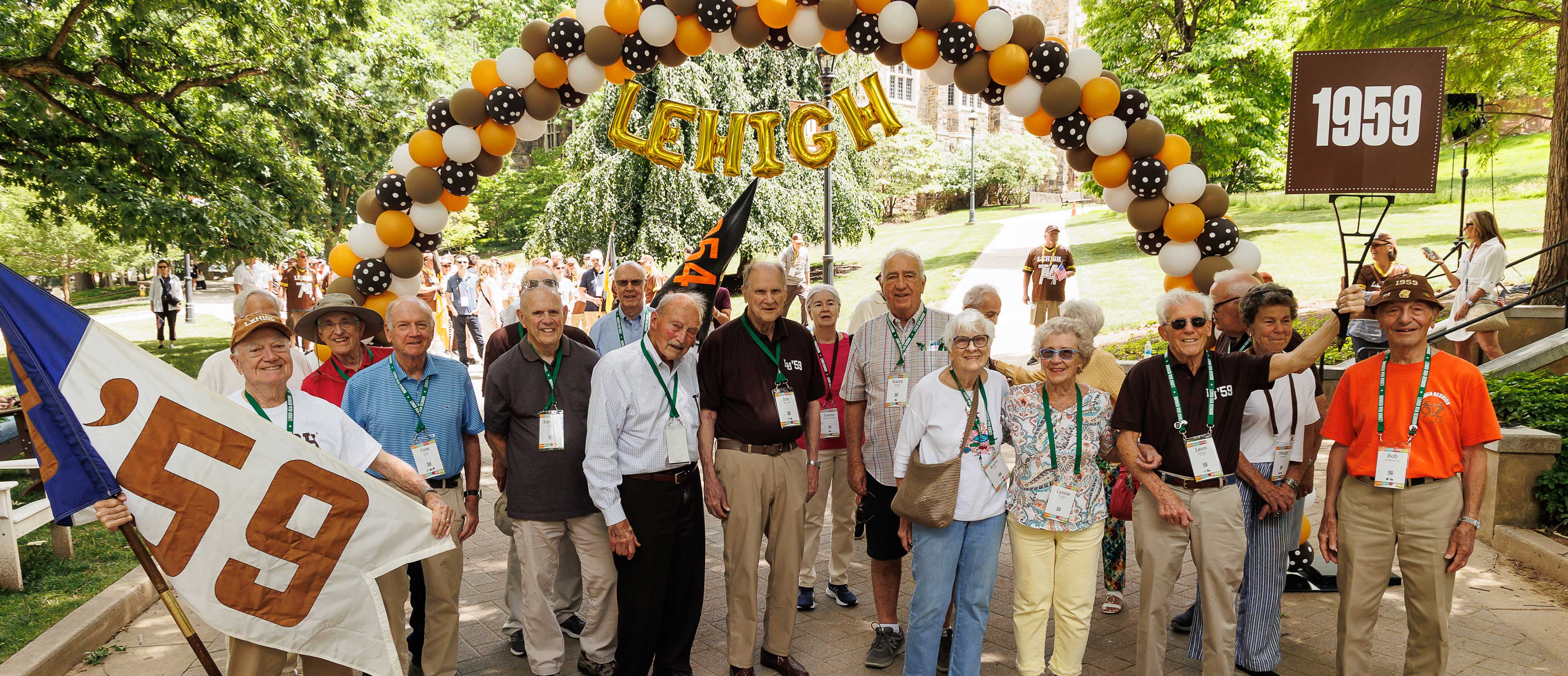 Men from the class of 1959 holding their flag and standing beneath the Lehigh balloon arch at Reunion.