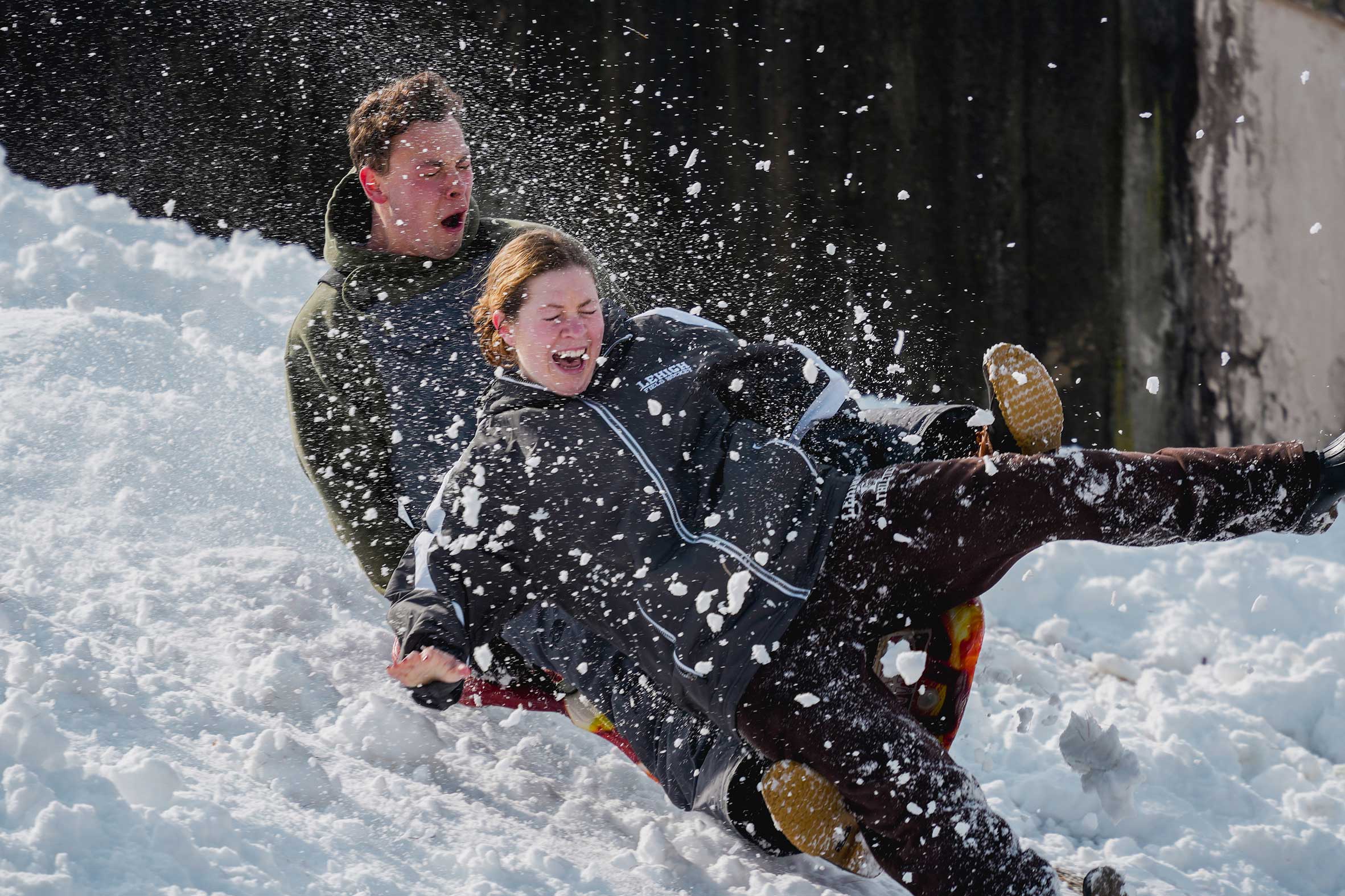 Two students sledding down a snowy hill together.