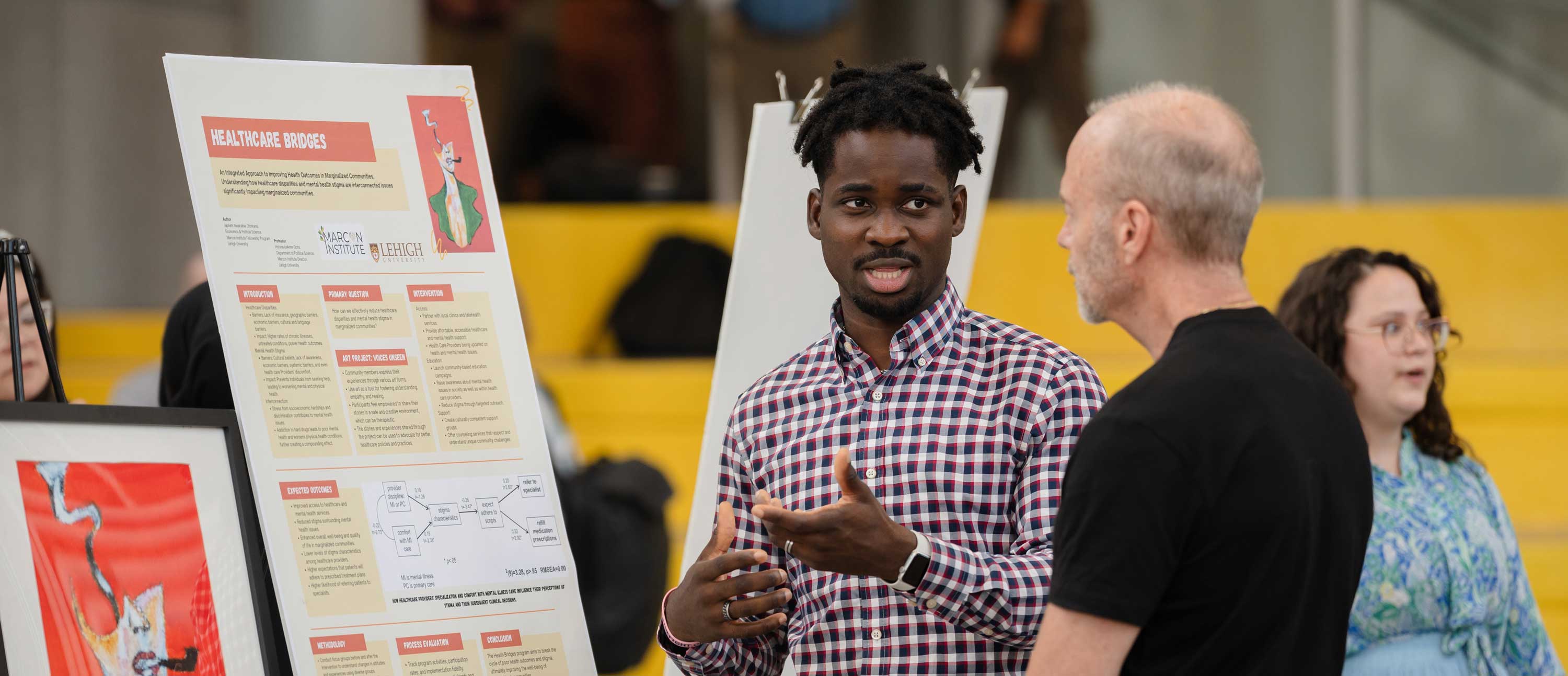 A male presenting student stands and presents his research project.