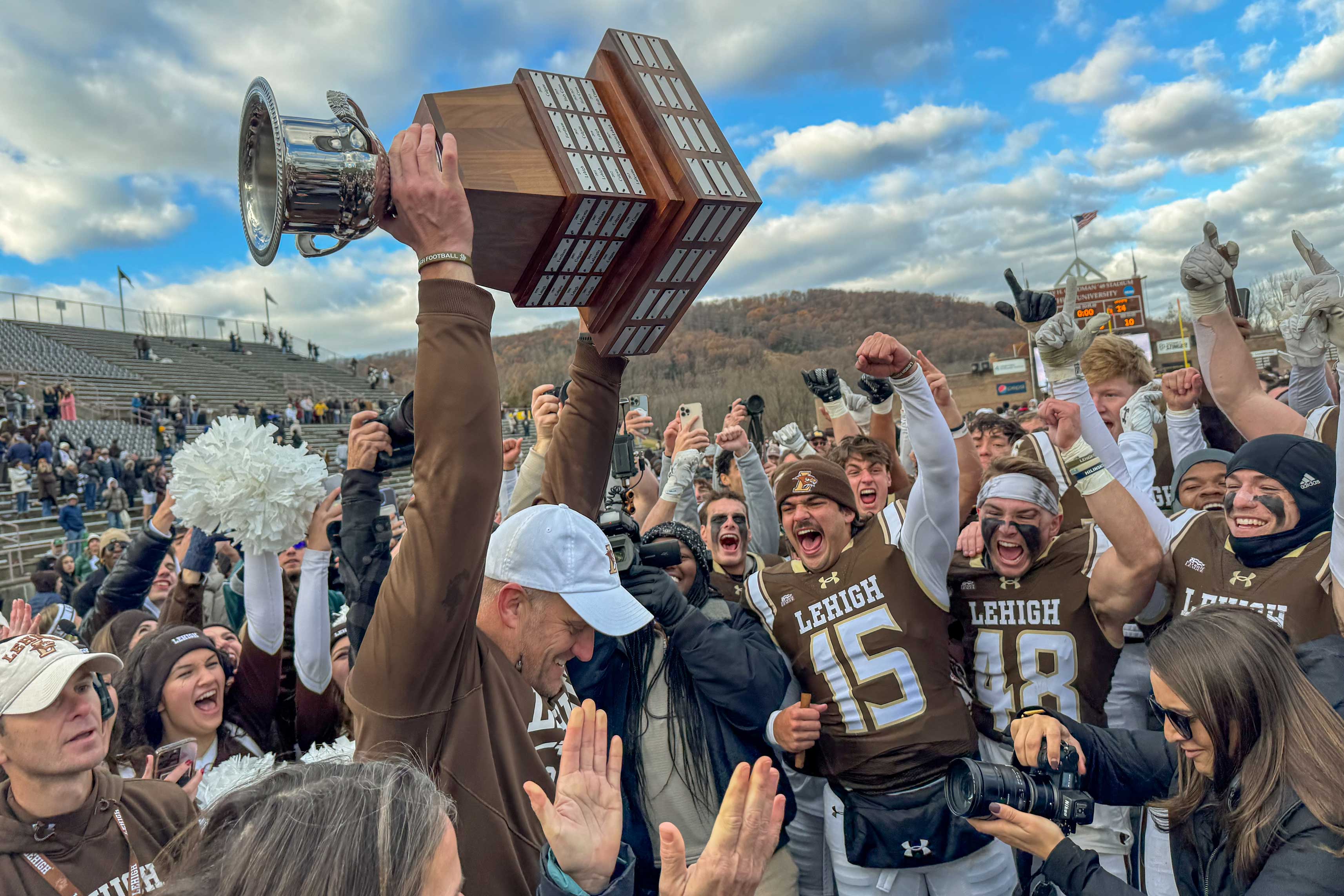 Coaches and football players from Lehigh University holding their trophy above their heads.