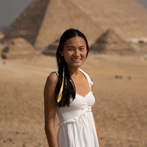 Claire in a white dress stands in front of the pyramids in Egypt
