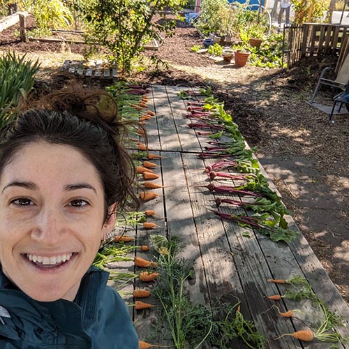 Mimi Bestwick taking a selfie in front of a table laden with carrots and radishes.