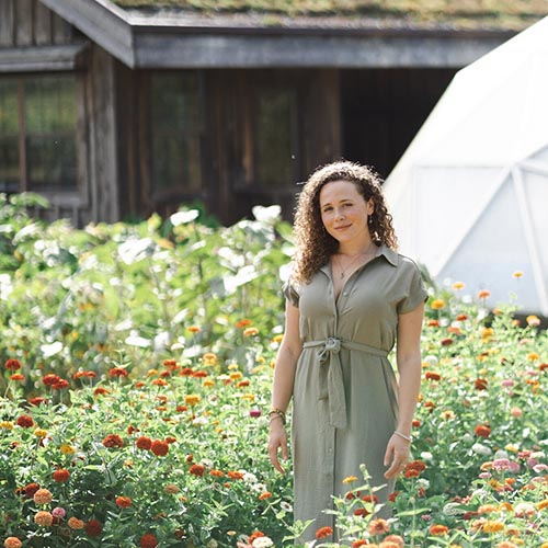 Nadine Clopton standing in a field of flowers in front of a bark-like structure.