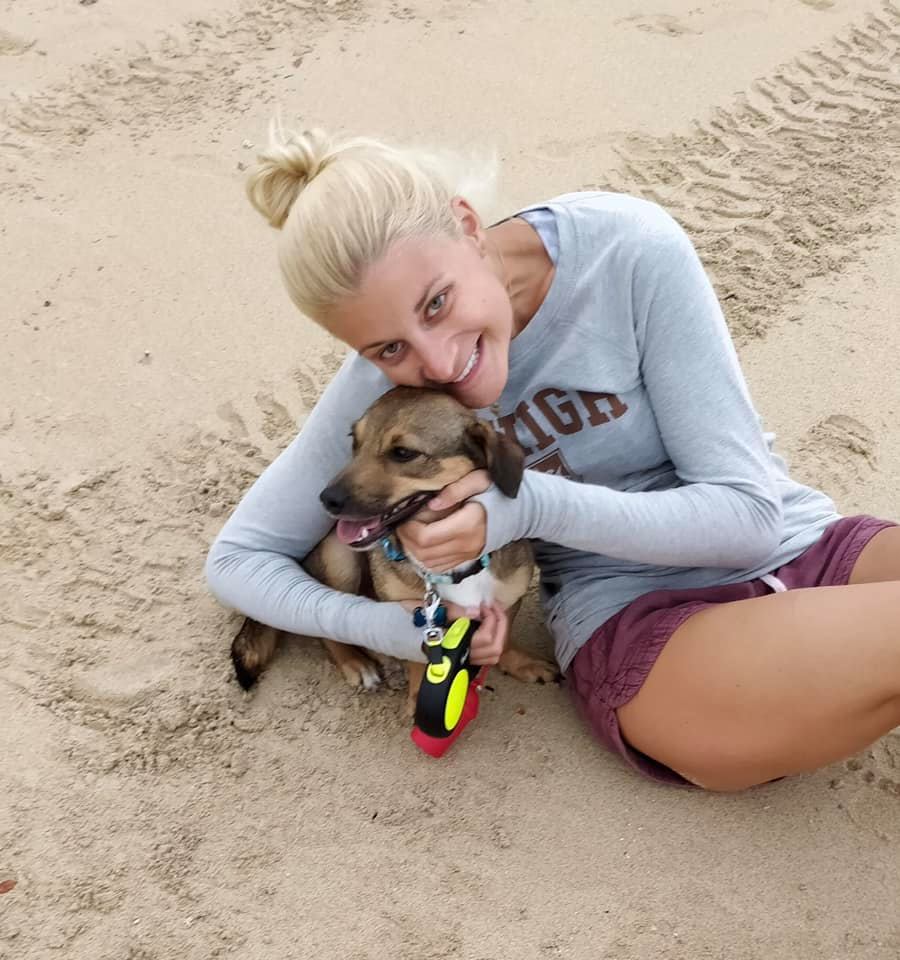Brittany Bartlett wearing a grey lehigh shirt and maroon shorts snuggles her daschund /terrier mix dog, Kai, on the beach.