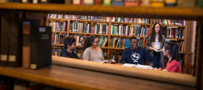 A group of students sitting between stacks of books studying.