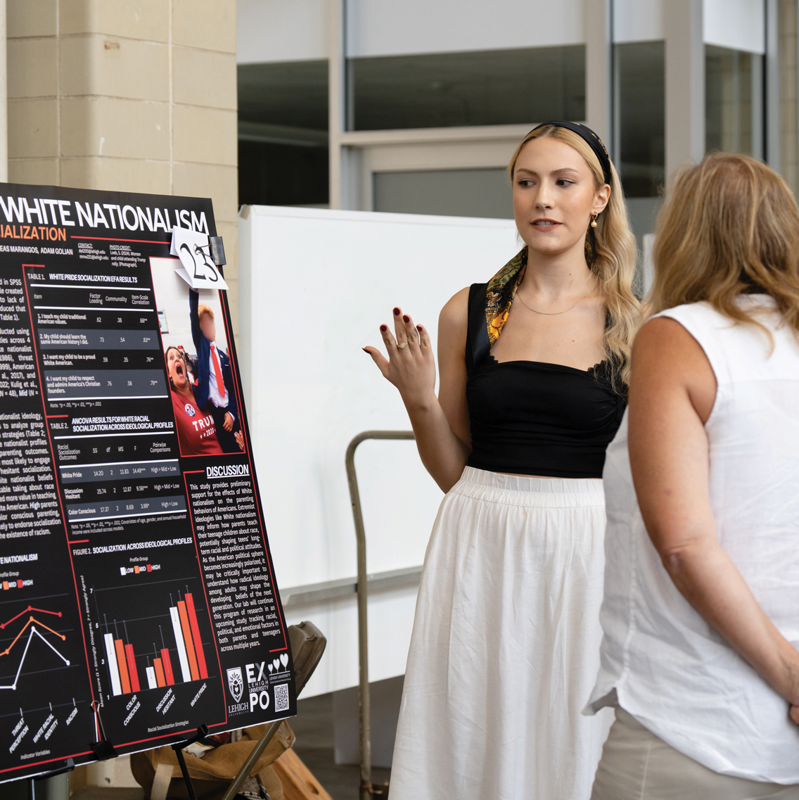 A Female student stands next to a poster board and explains her project.