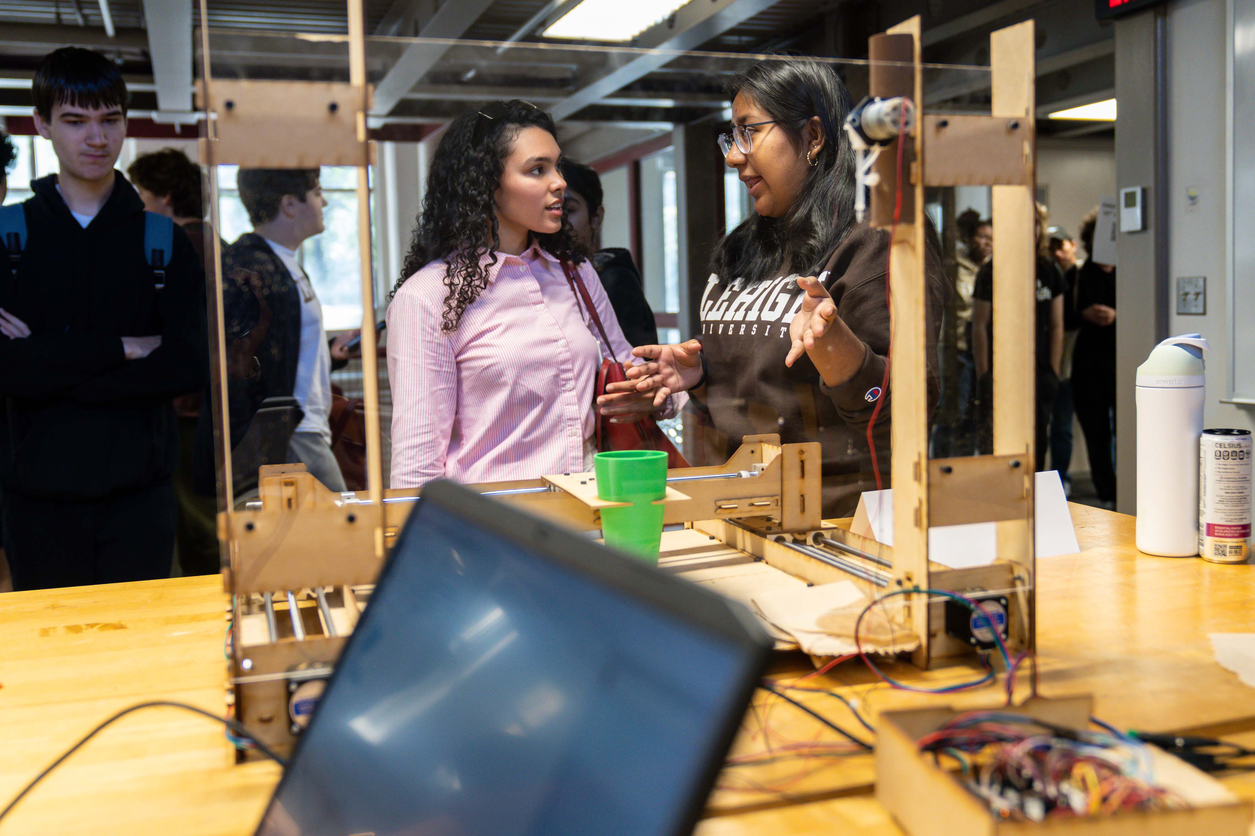 Two female students showcase their engineering project in the foreground
