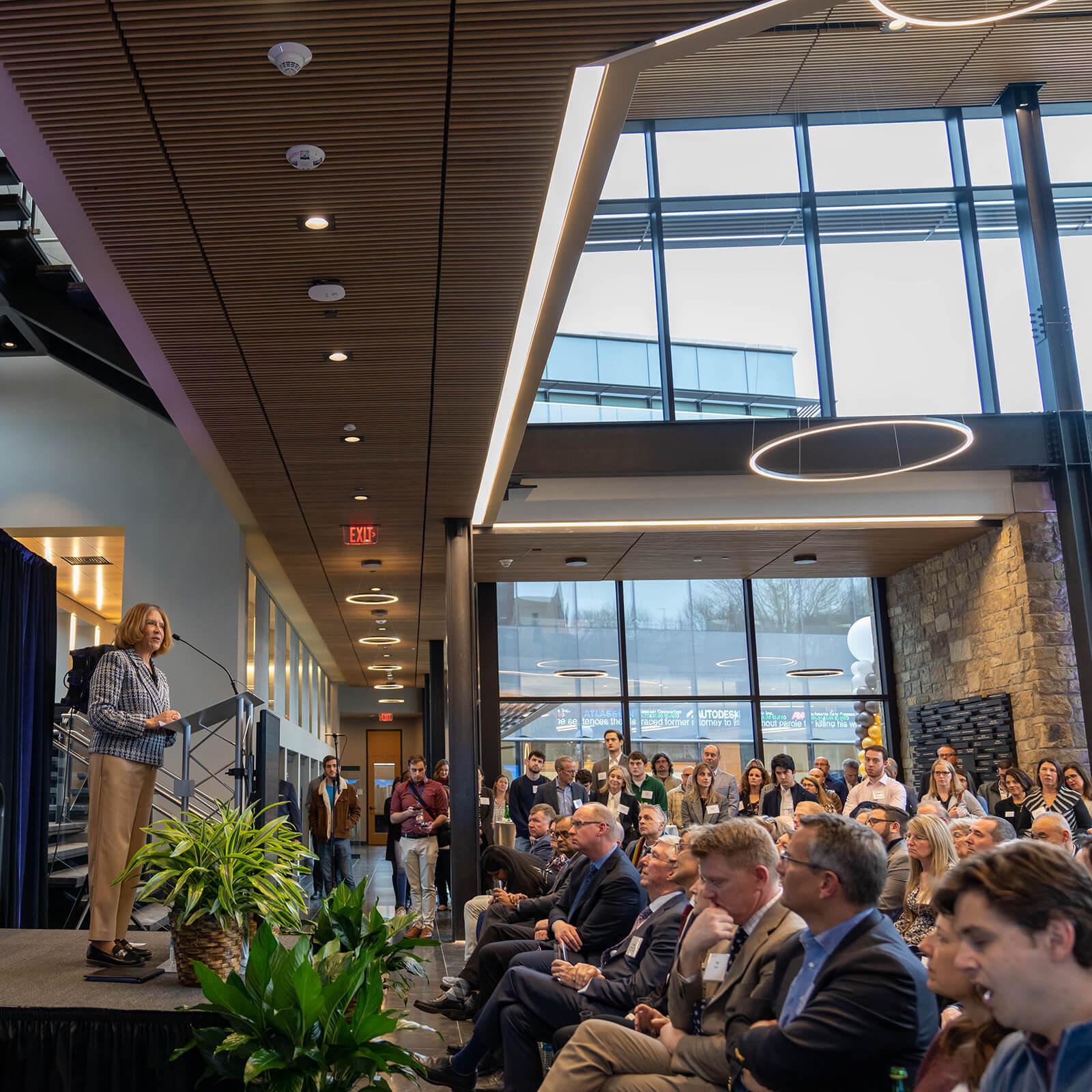 Dean Philips stands on a stage in front of a seated assembly in the lobby of the Business Innovation Building.