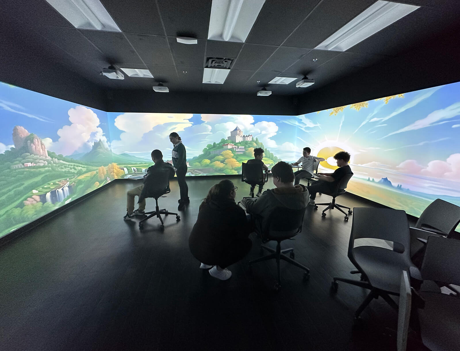 A dark room illuminated with 360-degree monitors showing an animated kingdom on a hill and sunny skies with fluffy clouds.