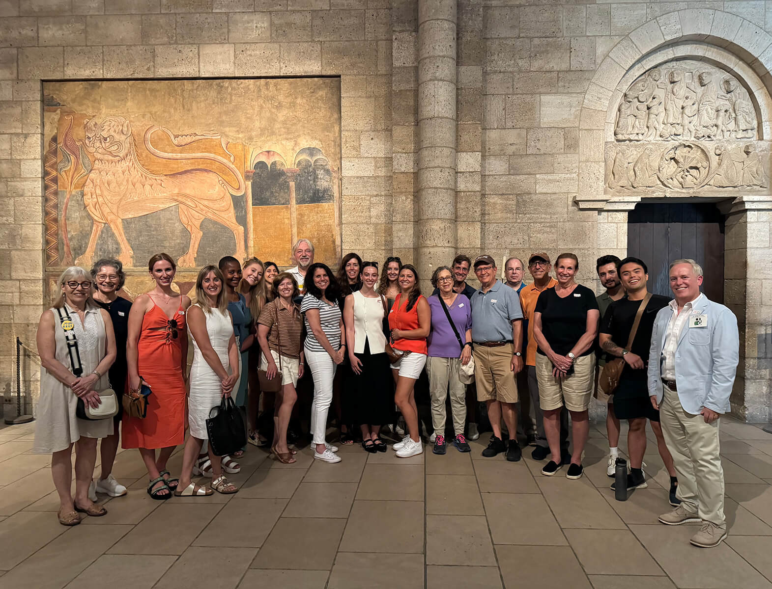 A large group of tourists stand together posing for a photo in a stone-walled museum.