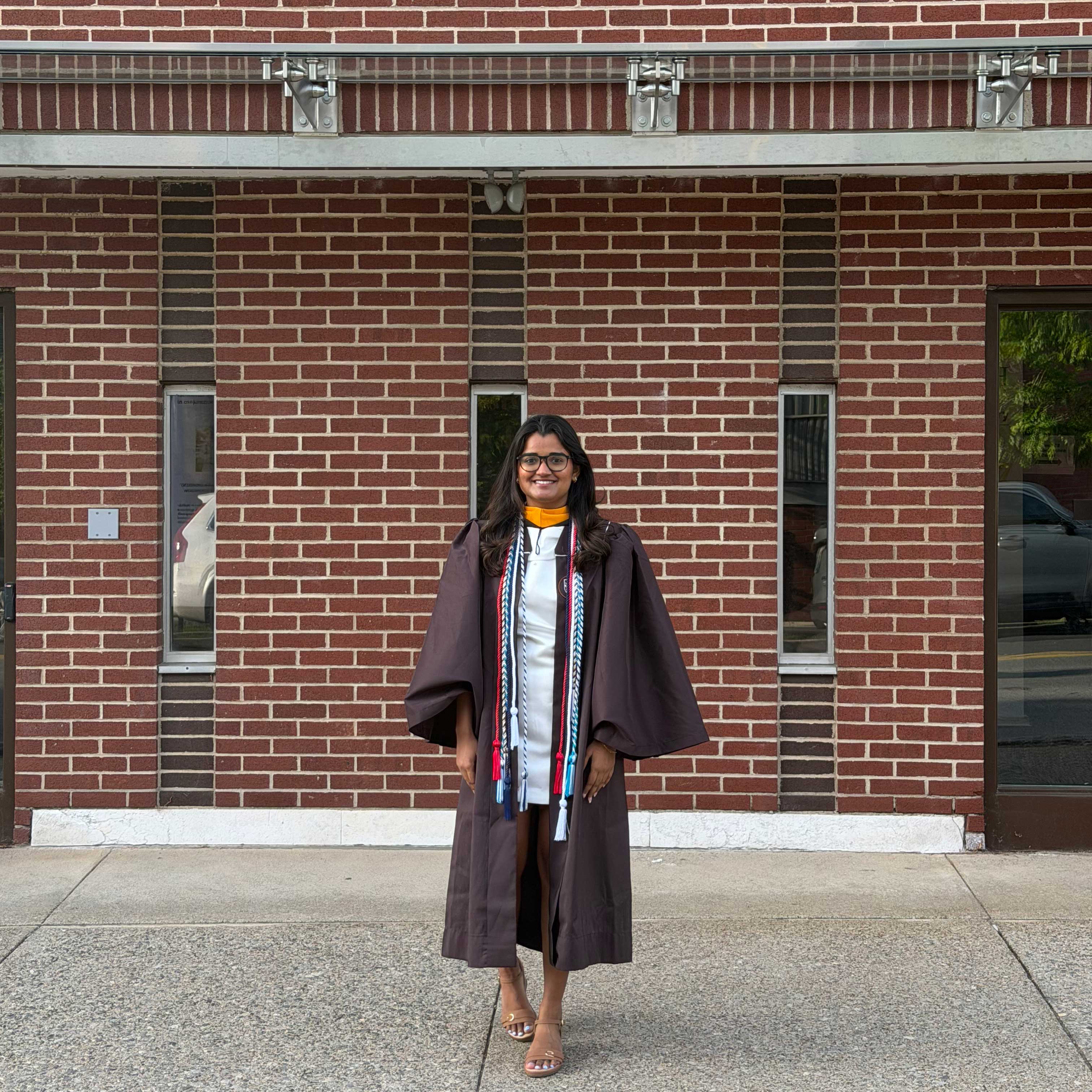Akanksha wears her graduation gown while smiling on campus.