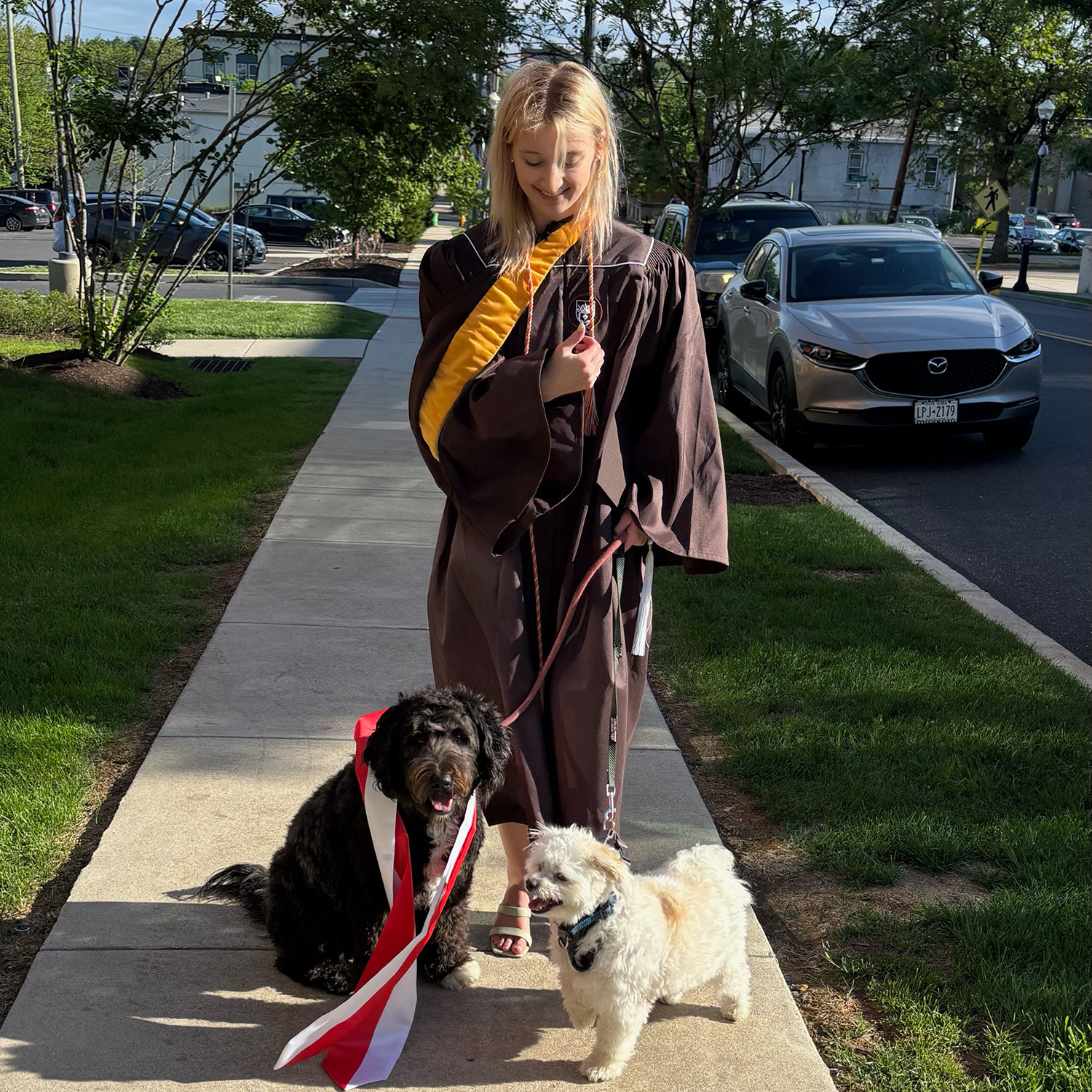 Alexandra with her two dogs smiles and gives a thumbs up wearing her Lehigh graduation gown and stole