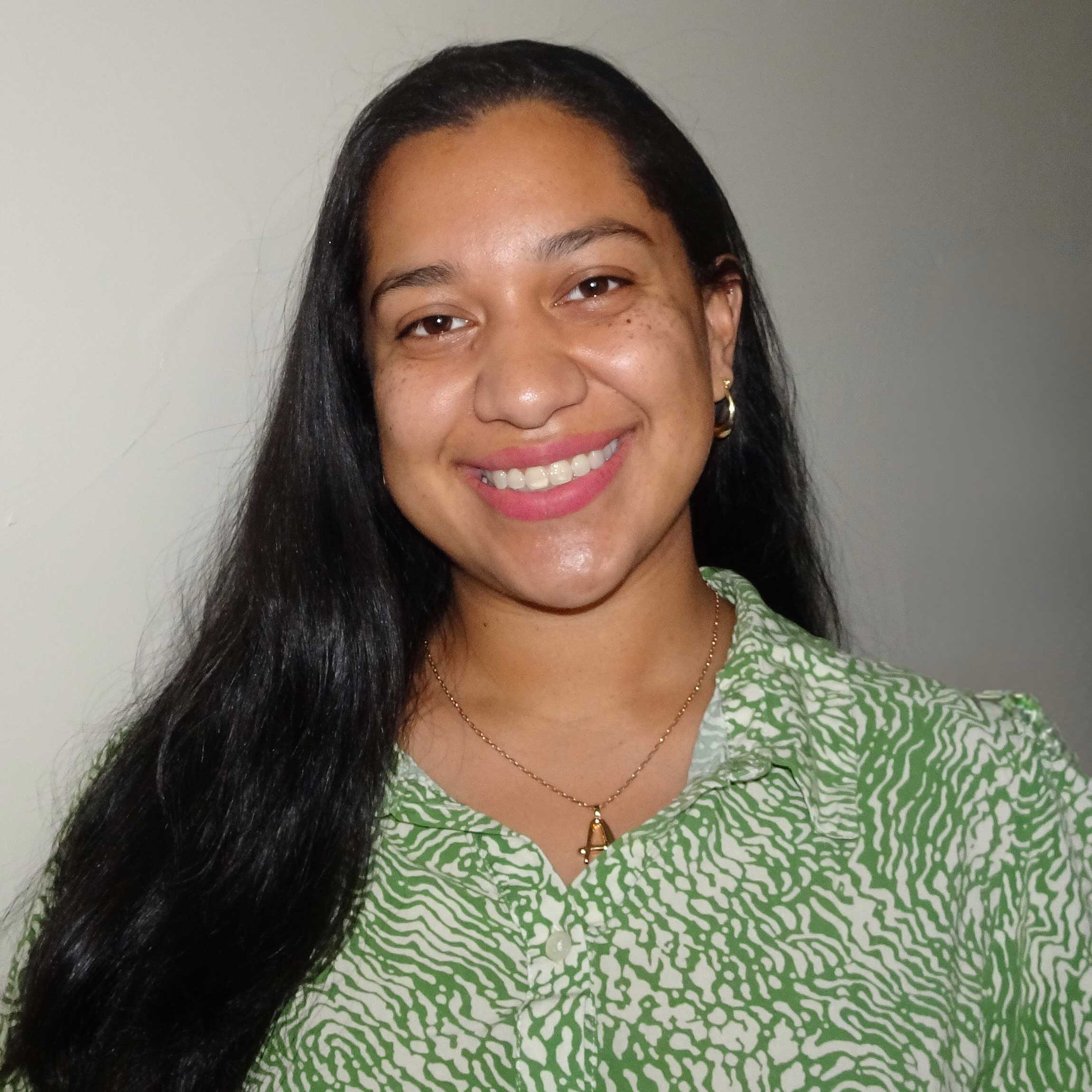 Alexandra wears a white and green blouse and a gold necklace. 