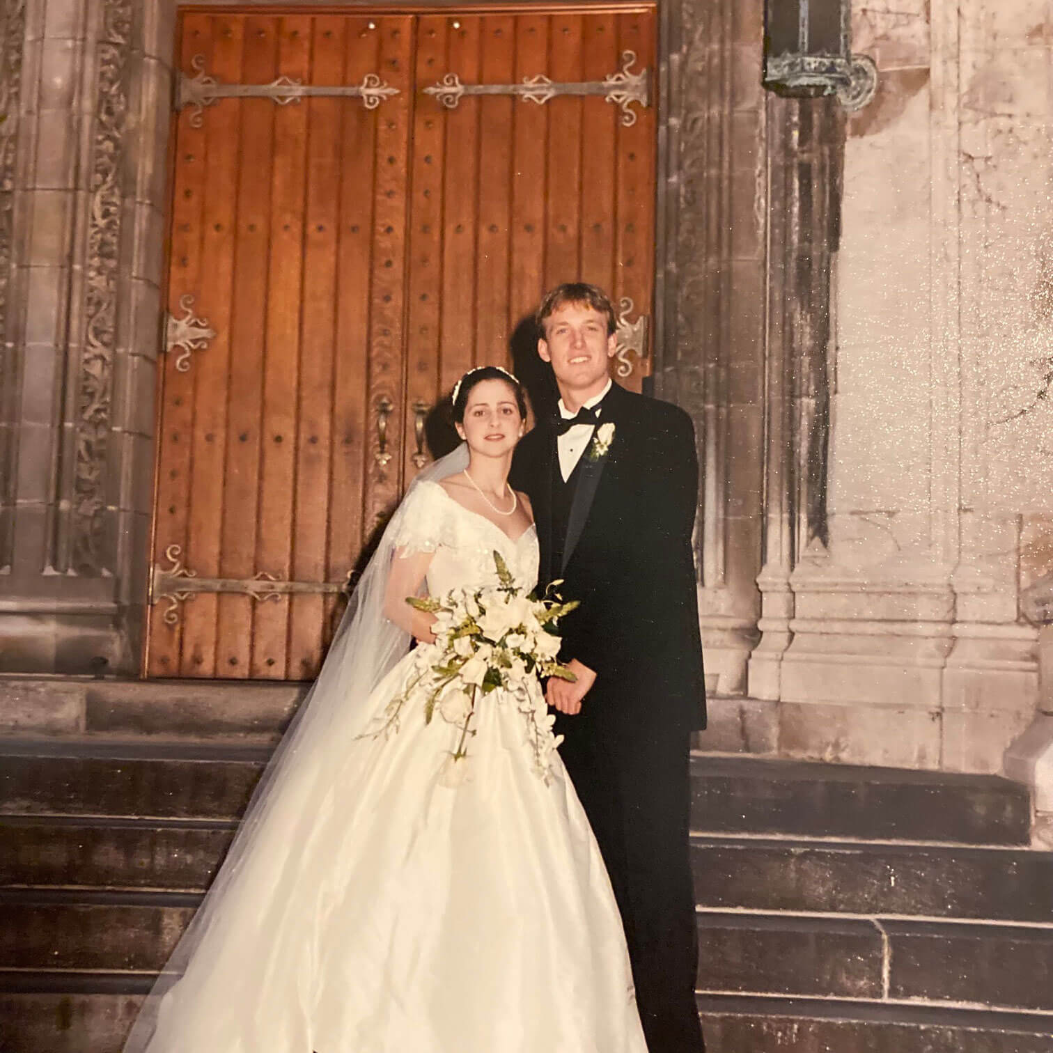 Jason and Ali Erk posing before a large wooden door on Lehigh's campus after their wedding reception.