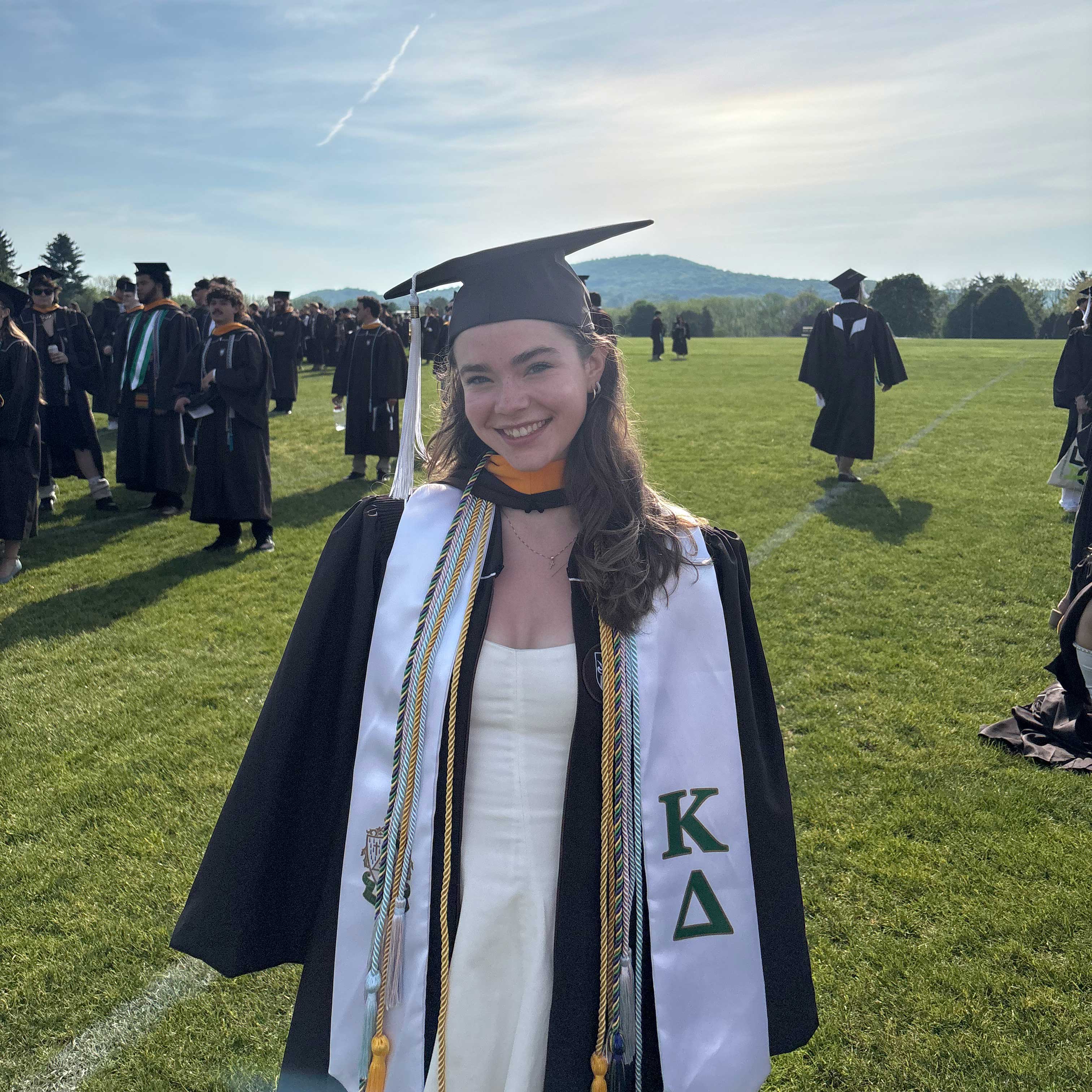 Anna Marie wears her cap and gown at graduation over a white dress.