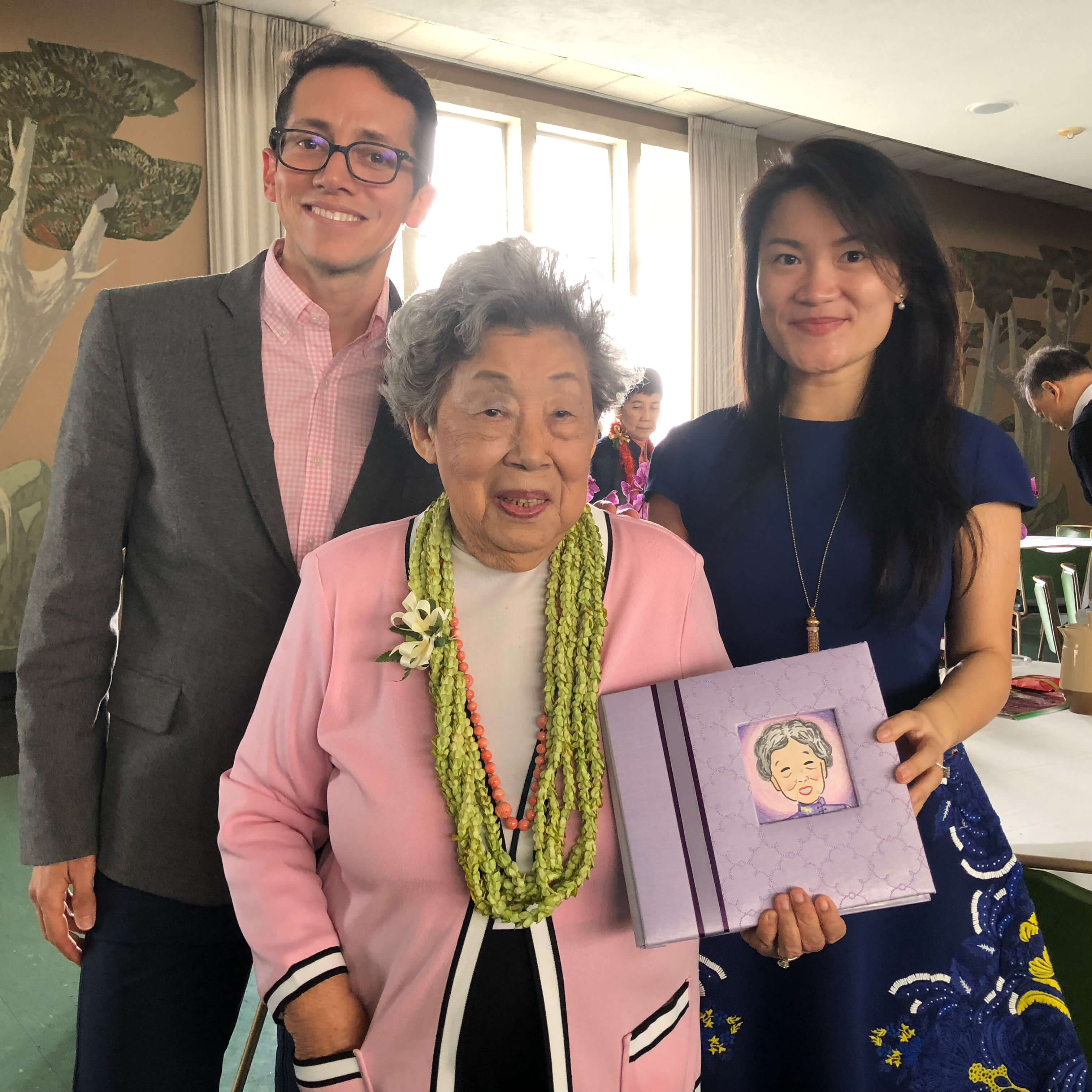 Louis and his wife stand with Roz, who holds a small, lilac book with a drawing of herself on the cover—a birthday gift. 