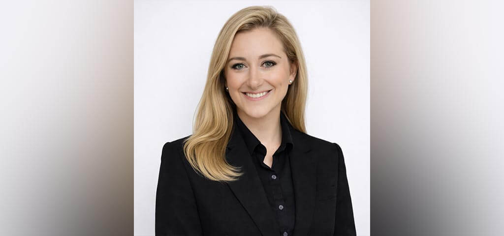 Ariana wears a black button up and blazer and smiles at the camera in a well-lit room