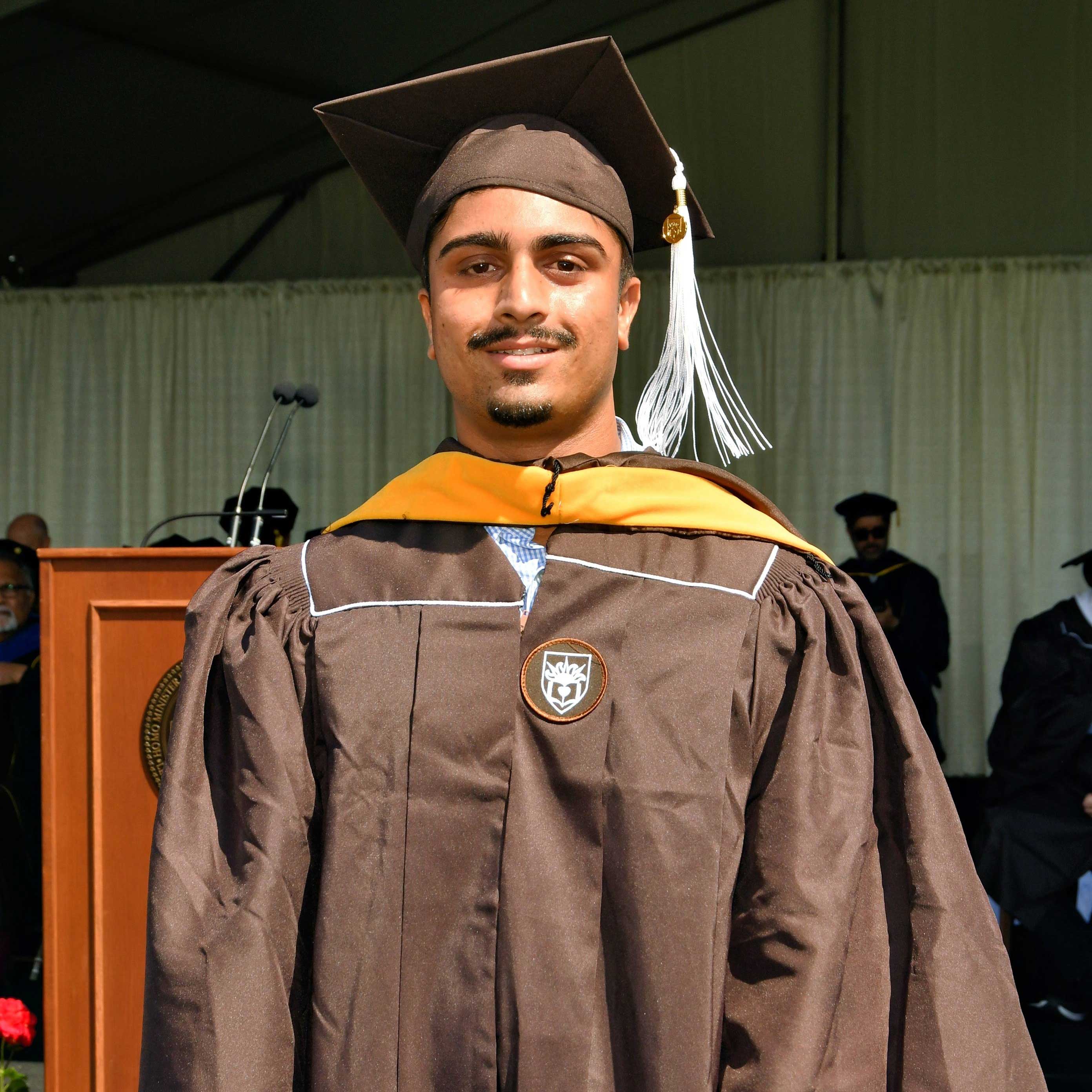 Arin wears his cap and gown at graduation and smiles.