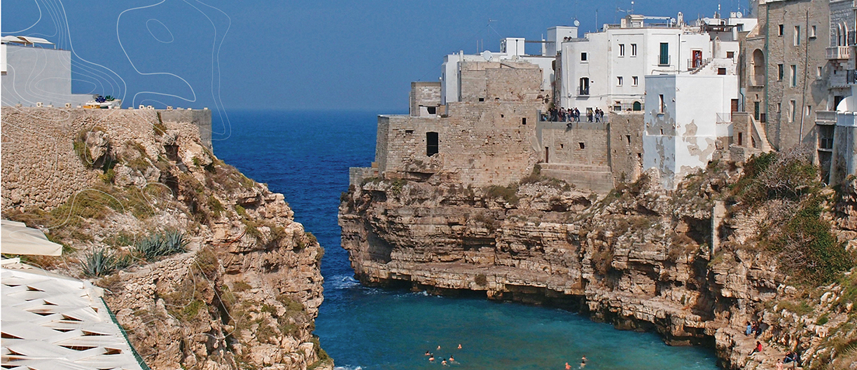 A scenic view of Puglia, Italy, featuring crystal-clear blue waters, craggy cliffs, and old buildings on the coastline.