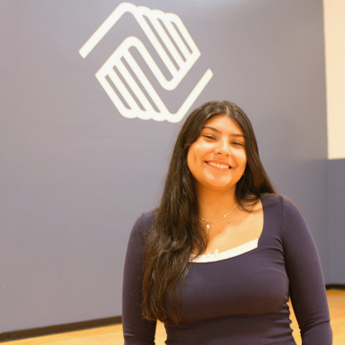 Indira Alvarado ’26 stands below the logo of the Boys and Girls Club.