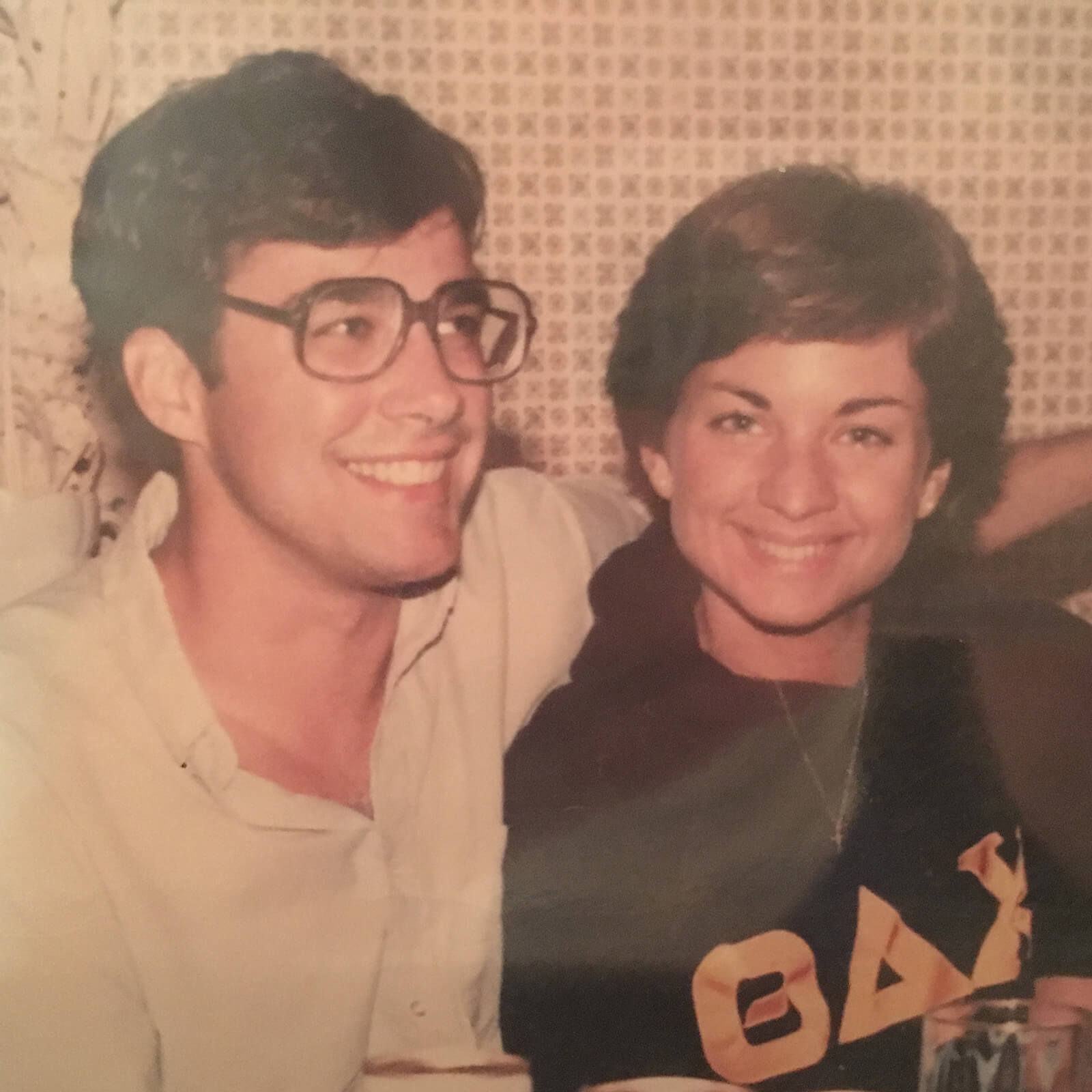 Tom Bartlett wearing large frame glasses with his arm around Fran in a faded photo from college.