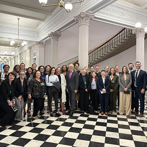 A group of men and women in professional outfits pose inside the White House