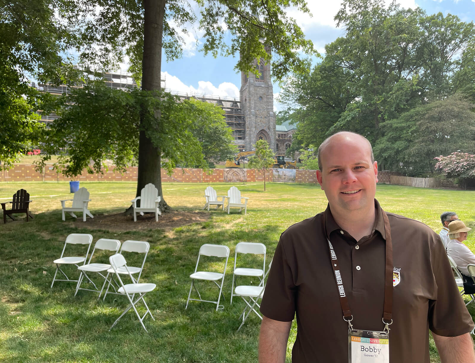 Alumnus stands in front of the University Center construction site wearing a brown Lehigh polo shirt lanyard with a name tag
