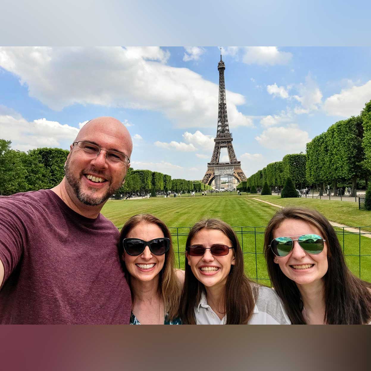 Brian and his family pose together and smile near the Eiffel Tower in Paris, France.