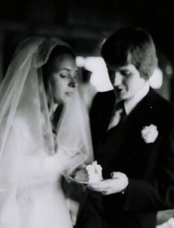 A blurry black and white photo of a bride and groom holding a plate of wedding cake. 