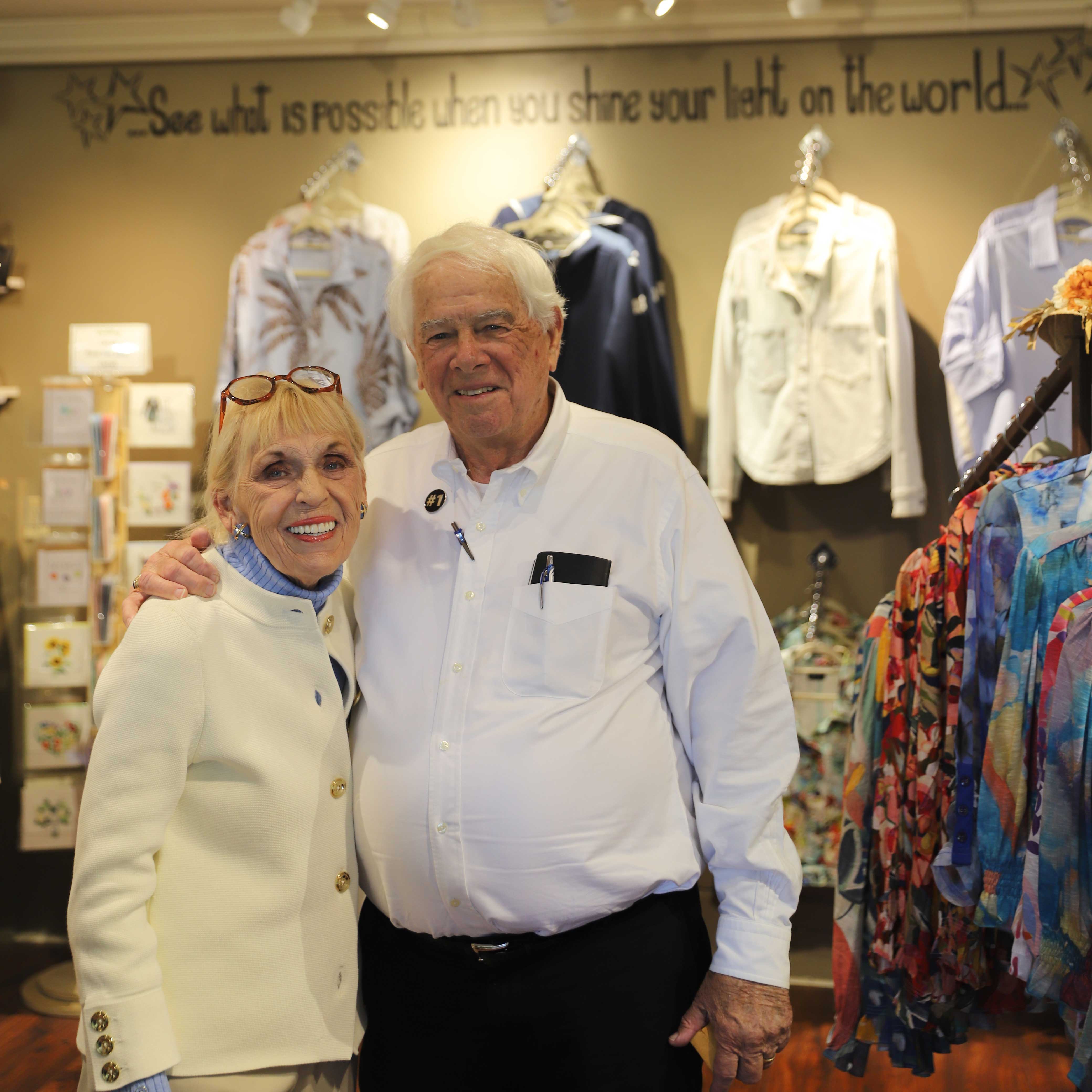 Bruce wraps an arm around Jo Ann while they stand in The Shoppe in the Hotel Bethlehem. Accessories are visible behind them.