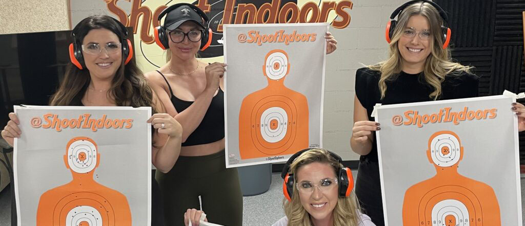 Four women wearing protective ear muffs holding up their paper shooting targets.